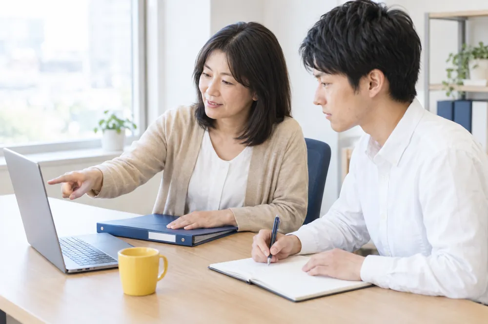 前の担当が新しい担当に、手順書とファイルを見せながら引き継いでいるイメージ