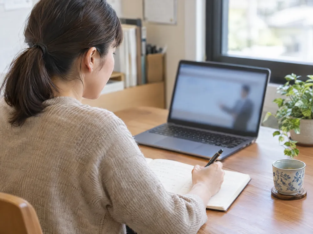 担当者が自分の机で、オンラインのレクチャーを受けながらノートにメモしているイメージ